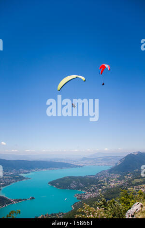 Parapendio volare sopra il lago di Annecy e il paesaggio di montagna nel cielo blu Foto Stock