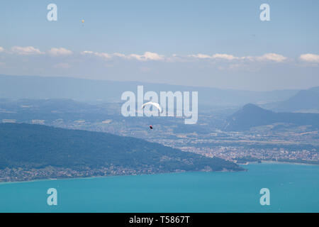 Parapendio volare sopra il lago di Annecy e il paesaggio di montagna nel cielo blu Foto Stock