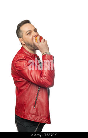 Un uomo in abiti eleganti di fronte a uno sfondo bianco morde un apple e guarda nella telecamera Foto Stock