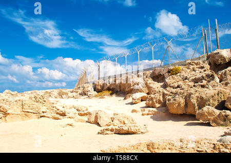 Recinzione militare da filo spinato su un terreno arido con numerosi massi di roccia su un giorno caldo in autunno Foto Stock
