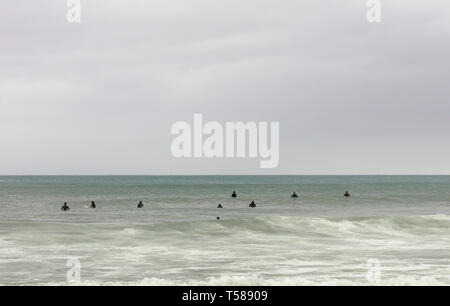 Surfers sui tavoli in attesa l'onda in un inverno nuvoloso giorno indossano un nero tuta in neoprene, spazio libero per il testo sulla parte superiore Foto Stock