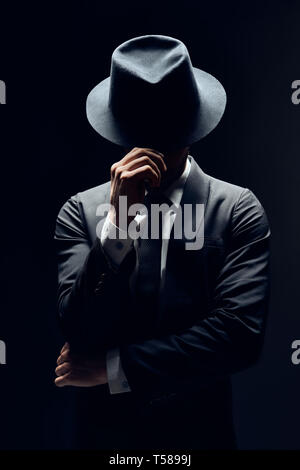 Uomo in tuta volto nascosto dietro il suo cappello isolato su sfondo scuro. segreto e in incognito concept Foto Stock