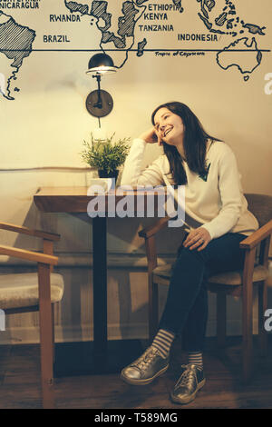 Immagine di un lifestyle ragazza a una tabella in un caffè vicino alla parete sotto una lampada elettrica di bere il caffè, le vere emozioni di una giovane e bella donna Foto Stock