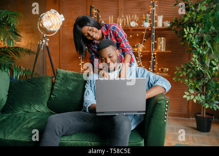 Nero giovane con laptop divertirsi sul divano Foto Stock