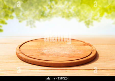 Tagliere di legno sulla scrivania con molla verde rami in background Foto Stock