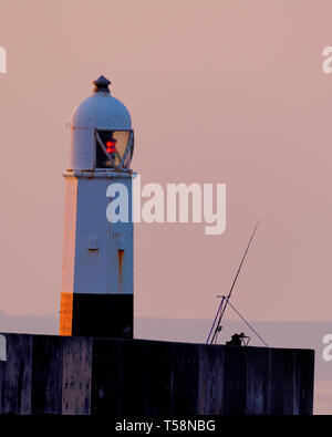 Una canna da pesca e stand silhouette contro il cielo di alba a Porthcawl faro UK. Foto Stock