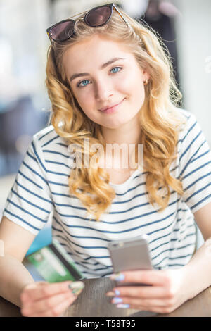 Giovane donna in cafe tenendo la carta di credito e utilizzando una cella, smart phone per lo shopping online. Foto Stock