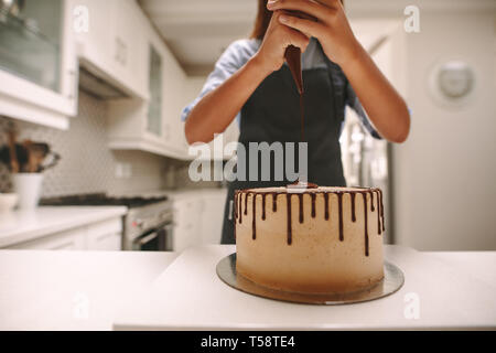 Pasticceria spreme cioccolata liquida da una sacca di tela da pasticceria su una torta su un supporto di legno. Donna fare una deliziosa torta a casa. Foto Stock