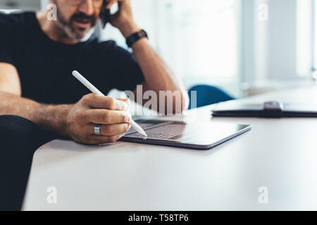 Uomo maturo parlando al cellulare e al lavoro sul suo digitale compressa. Imprenditore lavora in ufficio , focus sulla tavoletta digitale e penna. Foto Stock