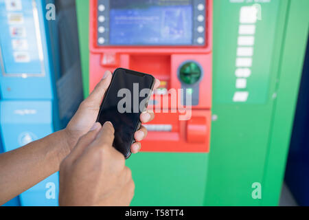 Uomo con telefono cellulare con schermo nero presso un bancomat. Codice di sicurezza di un Automated Teller Machine - Immagine Foto Stock