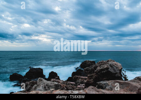 Drammatica nuvoloso vista mare di rocce e orizzonte al tramonto Foto Stock