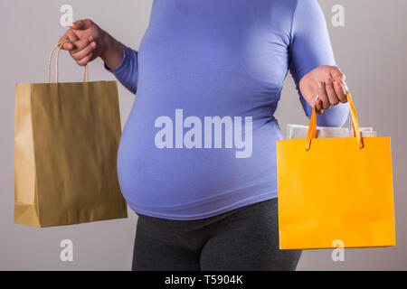 Immagine della donna incinta holding shopping bags su sfondo grigio. Foto Stock