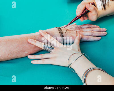 Henna dipinto a mano femminile. Henna dipinto artista disegna modelli su una mano. Araba e indiana pittura henné tradizioni Foto Stock