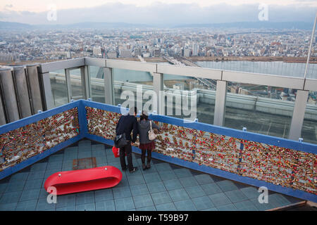 Coppia giovane attachting un amore lucchetto in la scherma di Umeda Sky Building observation deck. Osaka, Giappone Foto Stock