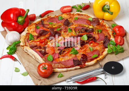 Piiza con un sacco di ingredienti e pizza coltello sul tavolo di legno still-life Foto Stock