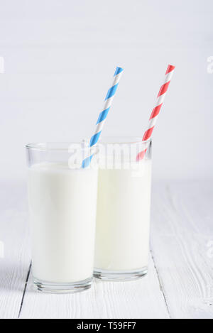 Due bicchieri di latte con il blu e il rosso spogliato cannucce di carta bianca sul tavolo in legno ancora vita Foto Stock