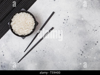 Tazza nera con bolliti basmati organico di riso al gelsomino con bacchette nere e il dolce di salsa di soia sul tappeto di pietra luce sul tavolo della cucina dello sfondo. Foto Stock