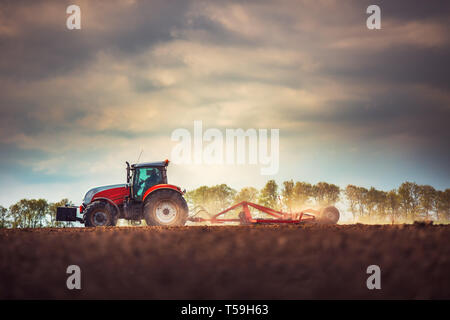 L'agricoltore nel trattore la preparazione di terra con il coltivatore del letto di semina Foto Stock