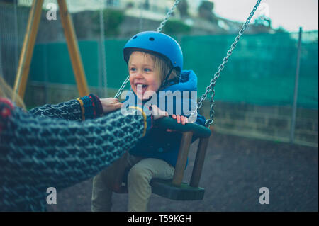 Un piccolo bimbo che indossa un casco è sull'altalena nel parco giochi Foto Stock