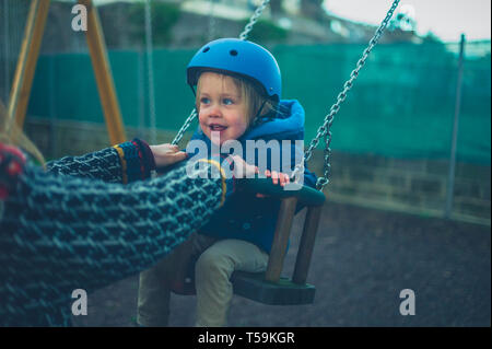 Un piccolo bimbo che indossa un casco è sull'altalena nel parco giochi Foto Stock