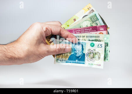 Un maschio di mano che trattiene le banconote in valute multiple con un cinque libbra dal Regno Unito nella parte anteriore. Foto Stock