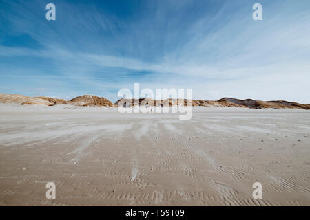 Ampia spiaggia di sabbia paesaggio durante la bassa marea con le colline sull orizzonte sotto moderata cielo nuvoloso e sentieri del vento sulla sabbia, Amrum, Germania Foto Stock