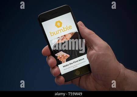 Un uomo guarda al suo iPhone che visualizza il logo Bumble (solo uso editoriale). Foto Stock