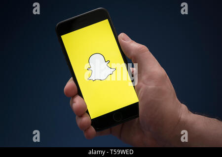 Un uomo guarda al suo iPhone che visualizza il logo Snapchat (solo uso editoriale). Foto Stock