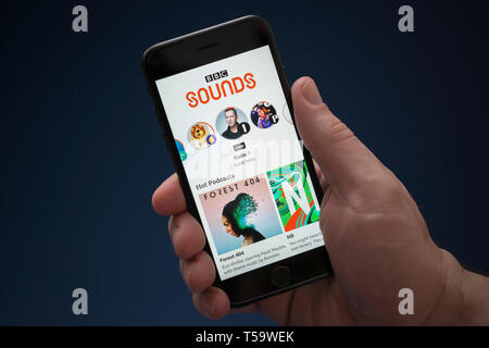 Un uomo guarda al suo iPhone che visualizza la BBC suoni logo (solo uso editoriale). Foto Stock