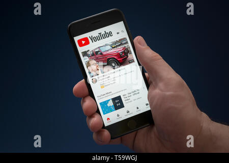 Un uomo guarda al suo iPhone che visualizza il logo di YouTube (solo uso editoriale). Foto Stock