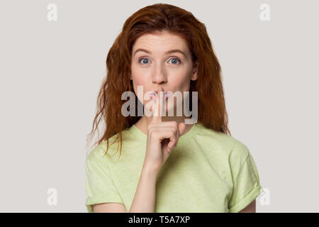 I Capelli rossi ragazza tenere il dito sulle labbra chiedendo il silenzio Foto Stock