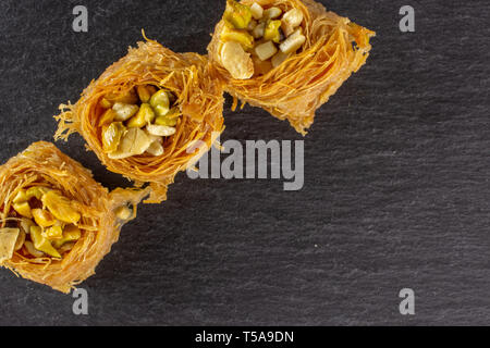 Gruppo di tre tutto il dolce baklava libanese pezzo bird nest varietà copyspace flatlay sulla pietra grigia Foto Stock