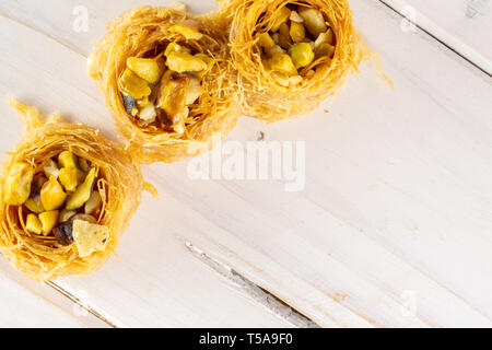 Gruppo di tre tutto il dolce baklava libanese pezzo bird nest varietà copyspace flatlay su legno bianco Foto Stock