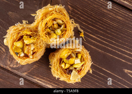 Gruppo di tre tutto il dolce baklava libanese pezzo bird nest varietà flatlay su legno marrone Foto Stock