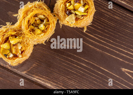 Gruppo di tre tutto il dolce baklava libanese pezzo bird nest varietà copyspace flatlay su legno marrone Foto Stock