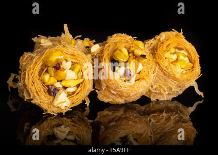 Gruppo di tre tutto il dolce baklava libanese pezzo bird nest varietà isolate su vetro nero Foto Stock