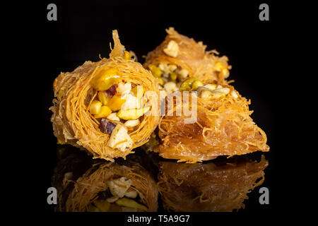 Gruppo di tre tutto il dolce baklava libanese pezzo bird nest varietà isolate su vetro nero Foto Stock