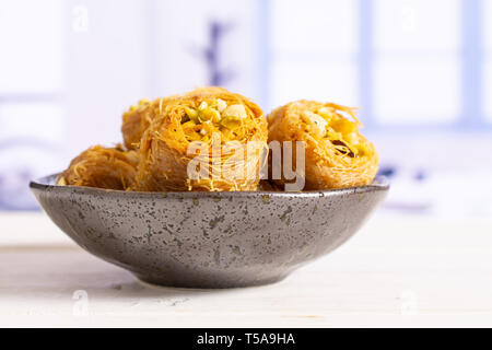 Sacco di tutta la dolce baklava libanese pezzo bird nest varietà su grigio piastra ceramica con finestra blu in una cucina bianca Foto Stock