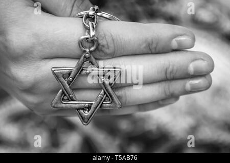 La mano di una giovane donna tenendo premuto un tasto catena con una stella di Davide, tradizionale simbolo ebraico. Concetto di immagine internazionale per il ricordo dell'Olocausto Foto Stock