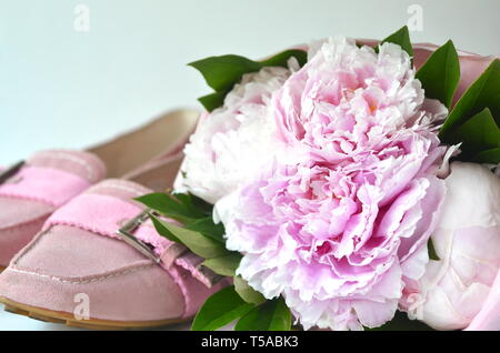 Luce rosa di pelle scamosciata ballerina flats scarpe con rosa pallido peonie bouquet avvolto in un tessuto di carta con spazio di copia Foto Stock