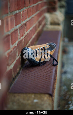 Vecchio puzzolente indossato classic sneaker perso su una strada di città Foto Stock