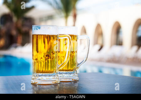 Due boccali da birra da piscina nel resort tropicale. Il turismo e il concetto di vacanza Foto Stock