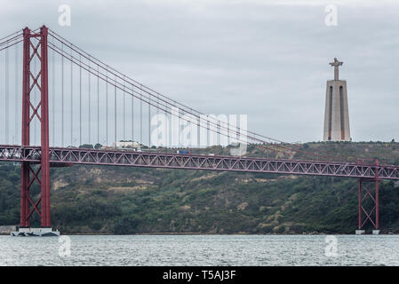 25 de Abril Bridge a Lisbona, Portogallo che connettono la città di Almada sul lato sinistro del fiume Tago. Vista con Cristo Re monumento Foto Stock