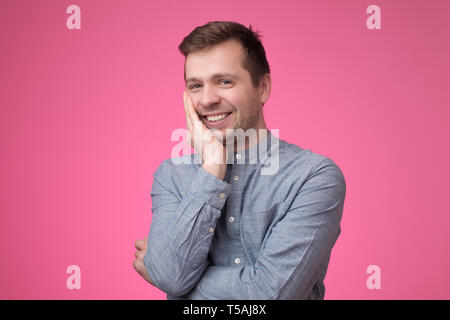 Sorridente giovane uomo caucasico mettendo la mano al suo mento Foto Stock