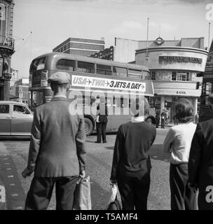 Anni sessanta, storico, persone che guardano un poliziotto dirigere il traffico come un autobus Routemaster tenta di fare un giro a sinistra in corrispondenza di una giunzione del tubo nella zona nord di Londra da un ramo della Midland Bank. Foto Stock