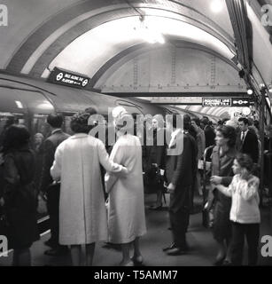 Anni sessanta, storico di passeggeri su un affollato platofrm circa a bordo di un treno di tubo sulla metropolitana di Londra, Londra, Inghilterra, Regno Unito. Foto Stock