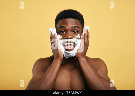 Funny Man con schiuma da barba sul suo volto fuori la sua lingua. close up photo isolati a sfondo giallo.Studio shot Foto Stock