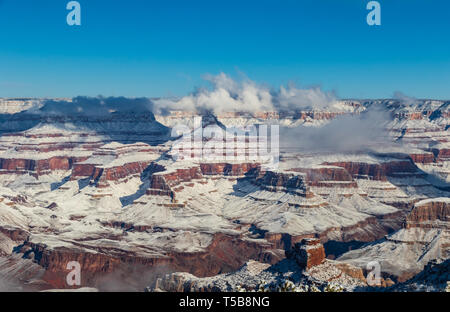 Il Grand Canyon in inverno dal south rim. Coperto di neve, nuvole aggrappati alla sommità del canyon. Cielo blu sopra. Foto Stock