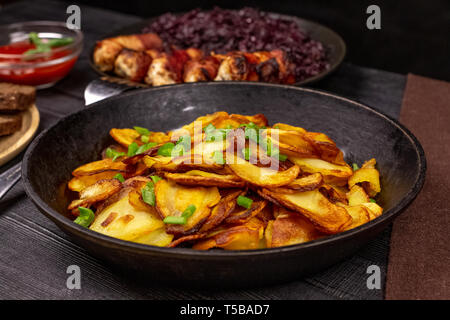 Patate fritte con chip verdi in una pentola, nella parte anteriore delle salsicce fatte in casa e stufati di cavolo nero a sfondo rustico. Foto Stock