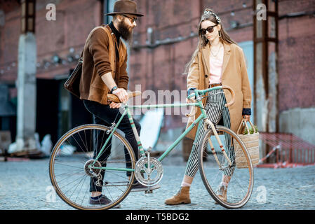 Elegante giovane uomo e donna avente una conversazione in piedi insieme con bicicletta retrò all'aperto su industriale di background urbano Foto Stock